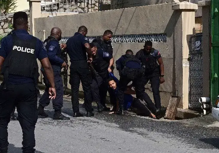 Caught: Port of Spain Task Force officers stand guard as their colleagues pull one of two shooting suspects out of a drain beneath the St Francois Valley Road, Belmont, opposite the St Francois Girls’ College on Friday.