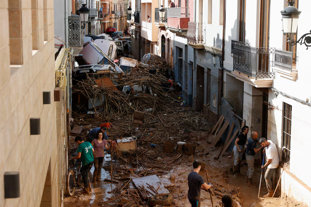 People work to clear a mud-covered street with piled up cars in the aftermath of torrential rains that caused flooding, in Paiporta, Spain, October 31, 2024.