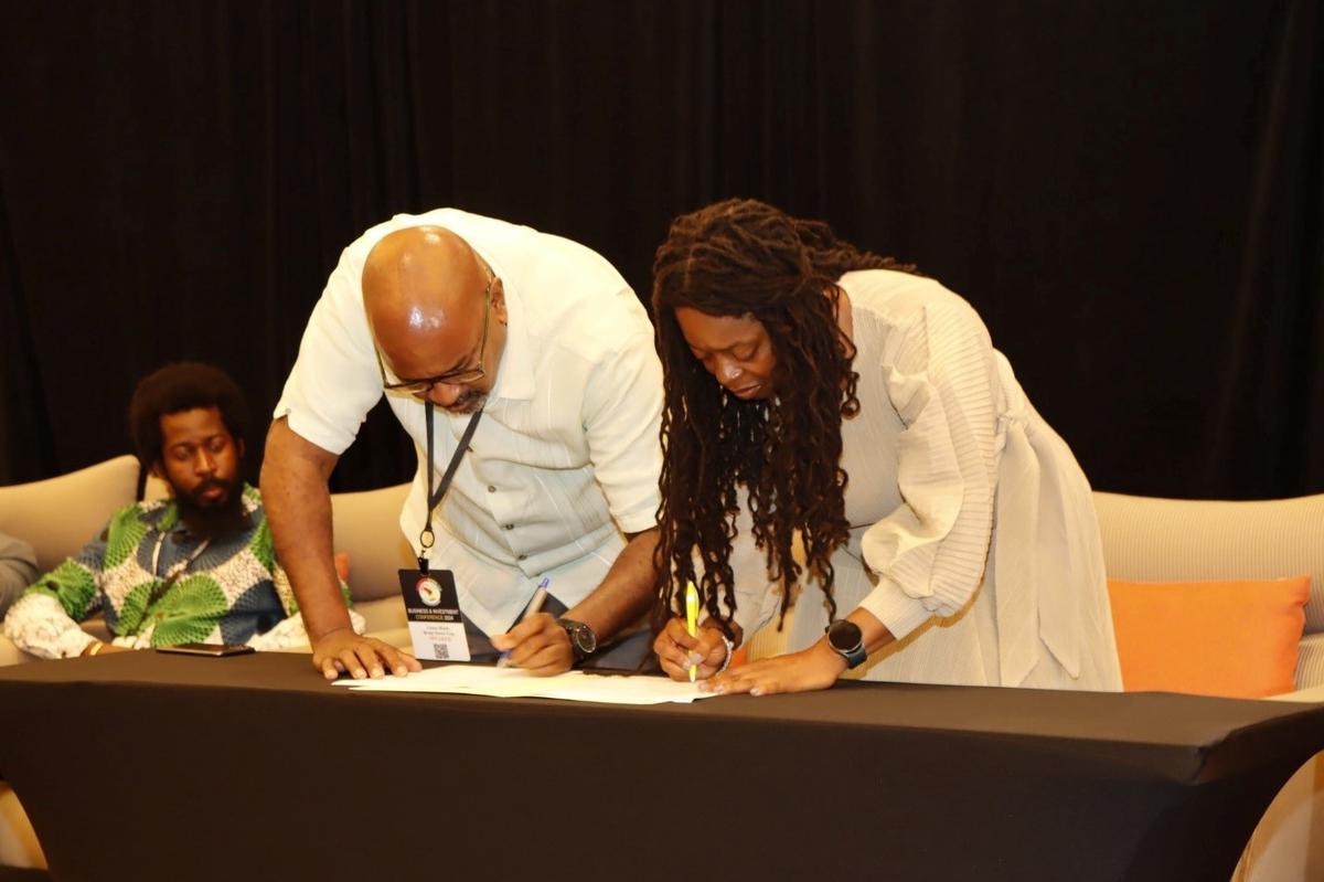 Stacey Mollison of the Global Opportunities Committee of the Atlanta Black Chambers (right) signing the MOU with Secretary of the Black Entrepreneurs Association (BEA) Lance Hinds; at left, seated is Chair of the BEA Rowen Willabus (NCN photo)